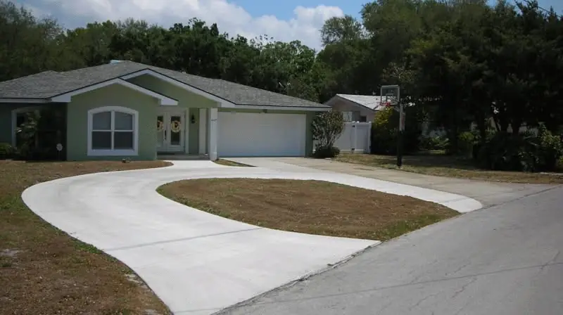 Broom-finished concrete driveway looping in front of a green Florida house