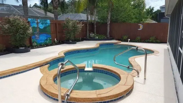 Freeform pool and spa with stamped coping and a tiled mural wall behind